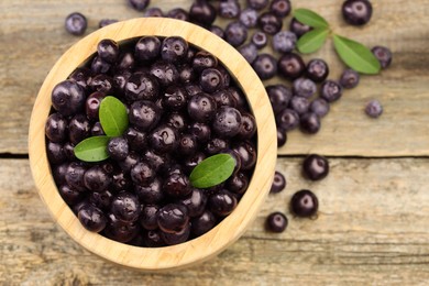 Ripe acai berries and leaves in bowl on wooden table, top view