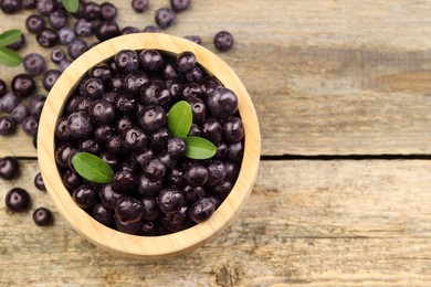 Photo of Ripe acai berries and leaves in bowl on wooden table, top view. Space for text