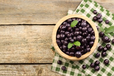 Ripe acai berries and leaves in bowl on wooden table, top view. Space for text