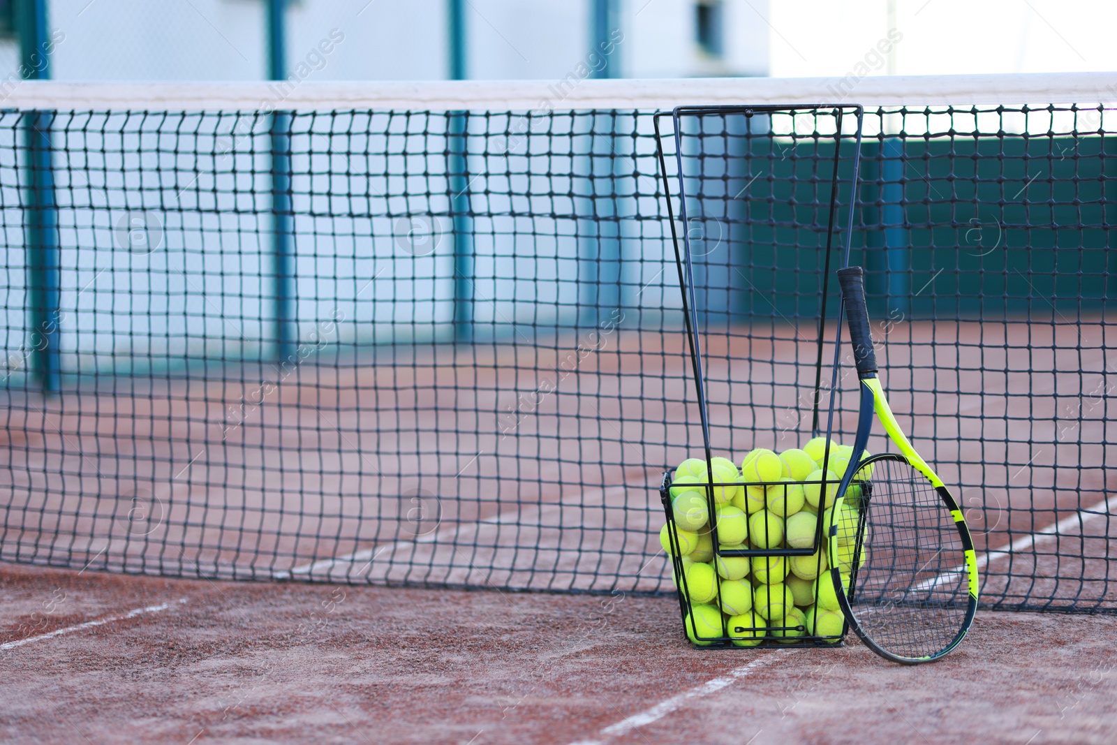 Photo of Tennis racket and balls in metal basket on court, space for text