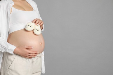 Photo of Young pregnant woman with pair of baby shoes on grey background, closeup. Space for text