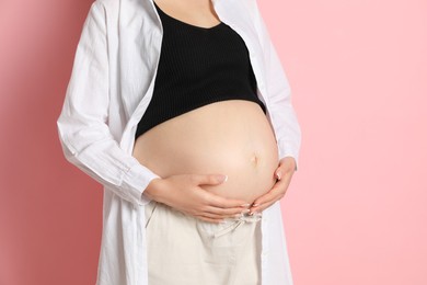 Photo of Young pregnant woman on pink background, closeup