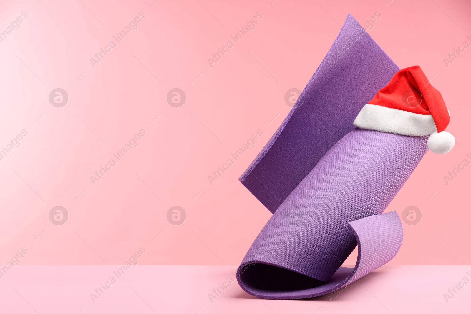 Photo of Yoga mat and Santa hat on pink background, space for text