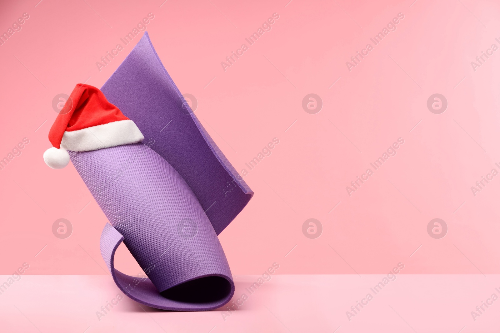 Photo of Yoga mat and Santa hat on pink background, space for text