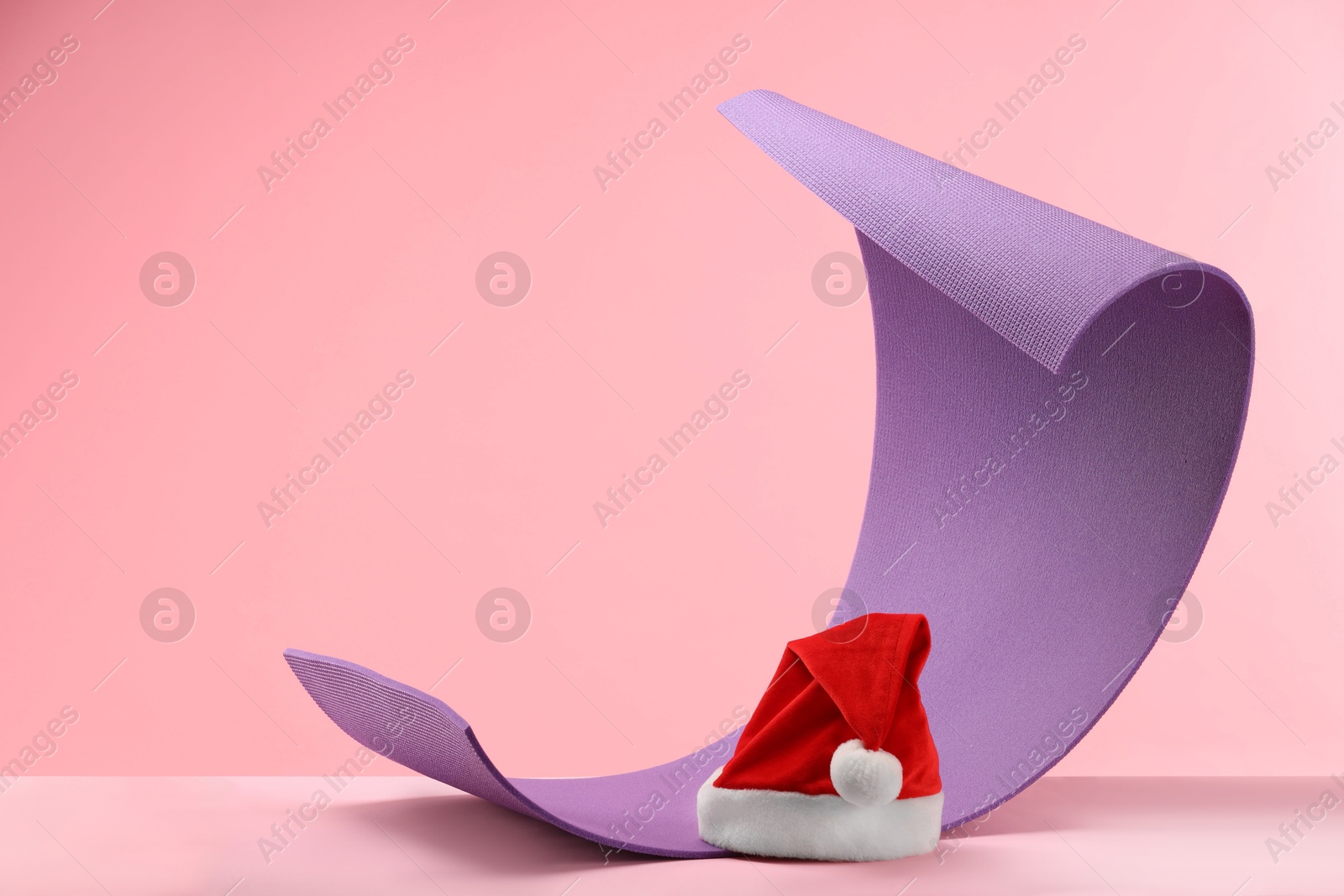 Photo of Yoga mat and Santa hat on pink background, space for text