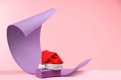 Photo of Yoga mat, block and Santa hat on pink background, space for text