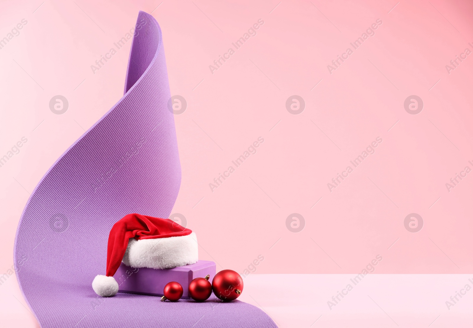 Photo of Yoga mat, Santa hat and baubles on pink background, space for text