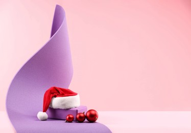 Photo of Yoga mat, Santa hat and baubles on pink background, space for text