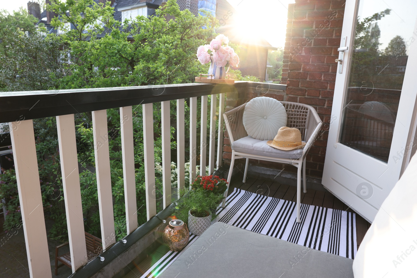 Photo of Vase with beautiful peonies on railings and chair at cozy balcony on sunny day