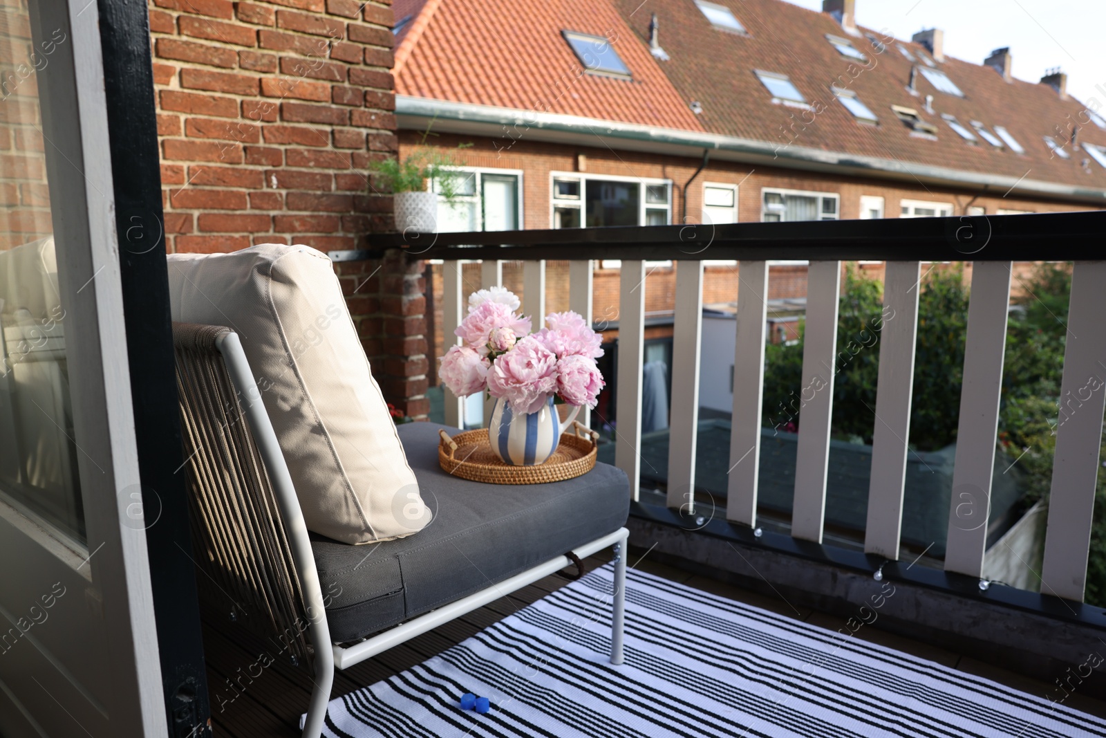 Photo of Vase with beautiful peony flowers on chair at cozy balcony