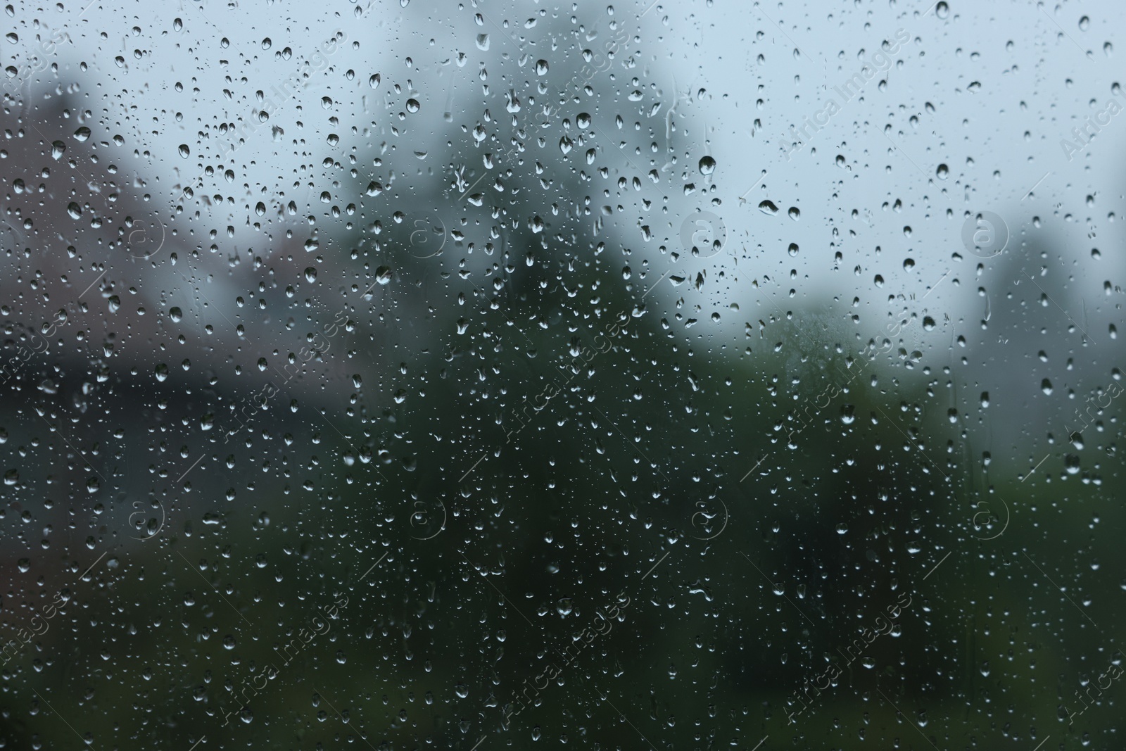 Photo of View on buildings through window with water droplets on rainy day, closeup