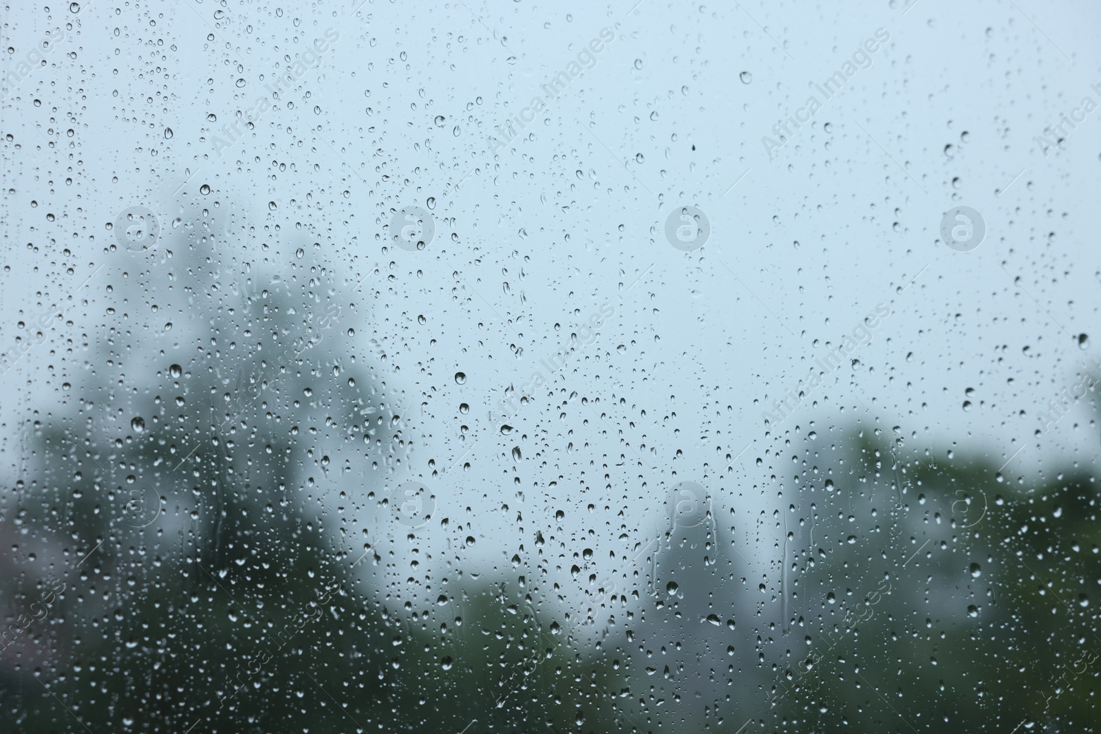 Photo of View on buildings through window with water droplets on rainy day, closeup