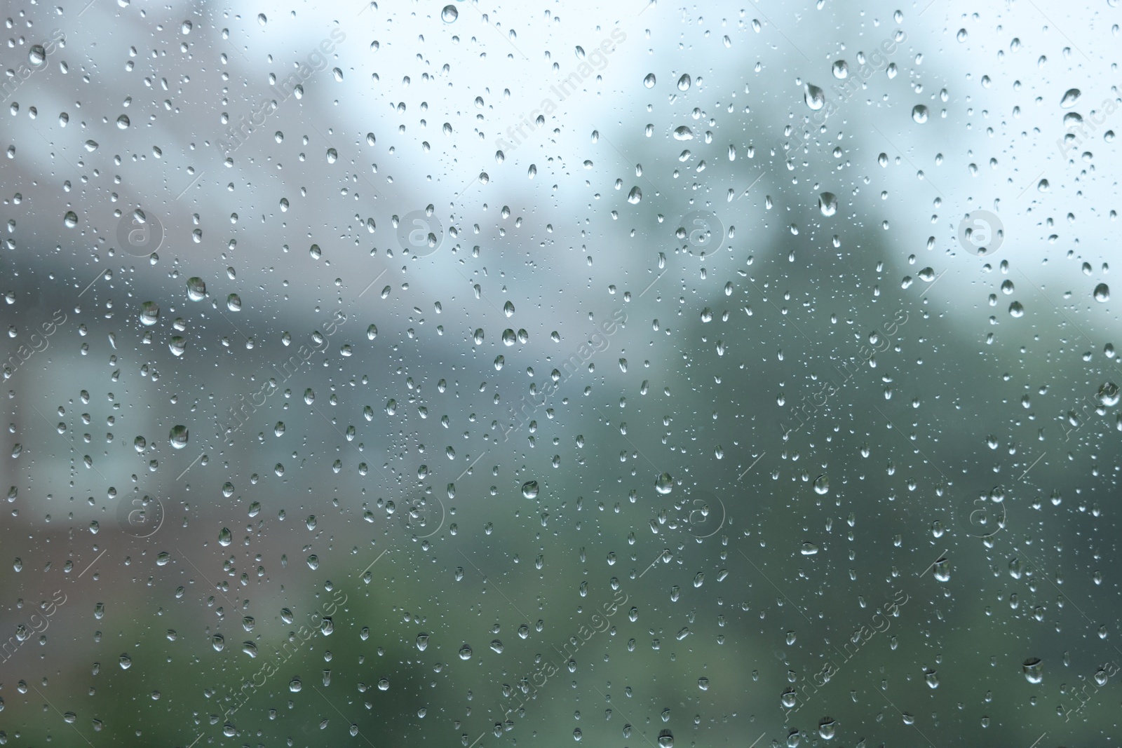 Photo of View on buildings through window with water droplets on rainy day, closeup