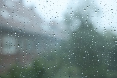 View on buildings through window with water droplets on rainy day, closeup