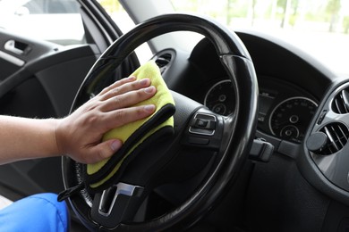 Man cleaning steering wheel with rag in car, closeup