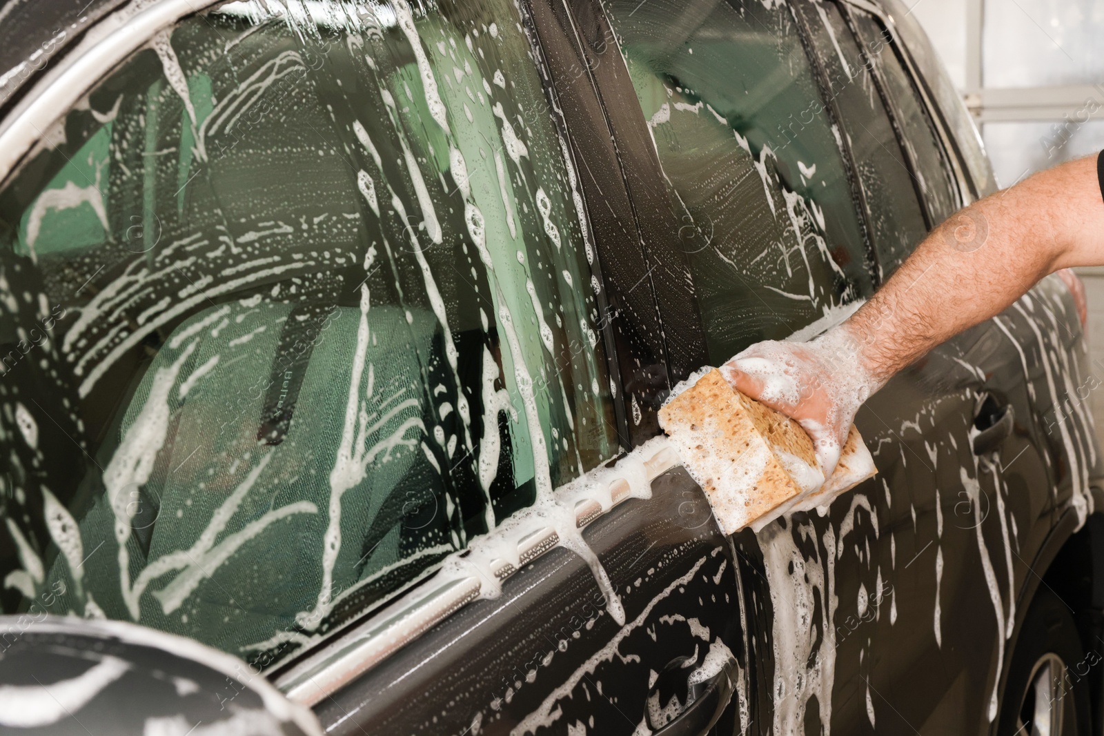 Photo of Man washing auto with sponge at car wash, closeup