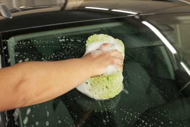 Photo of Man washing car windshield with sponge indoors, closeup