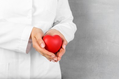 Doctor holding red heart on grey background, closeup. Space for text