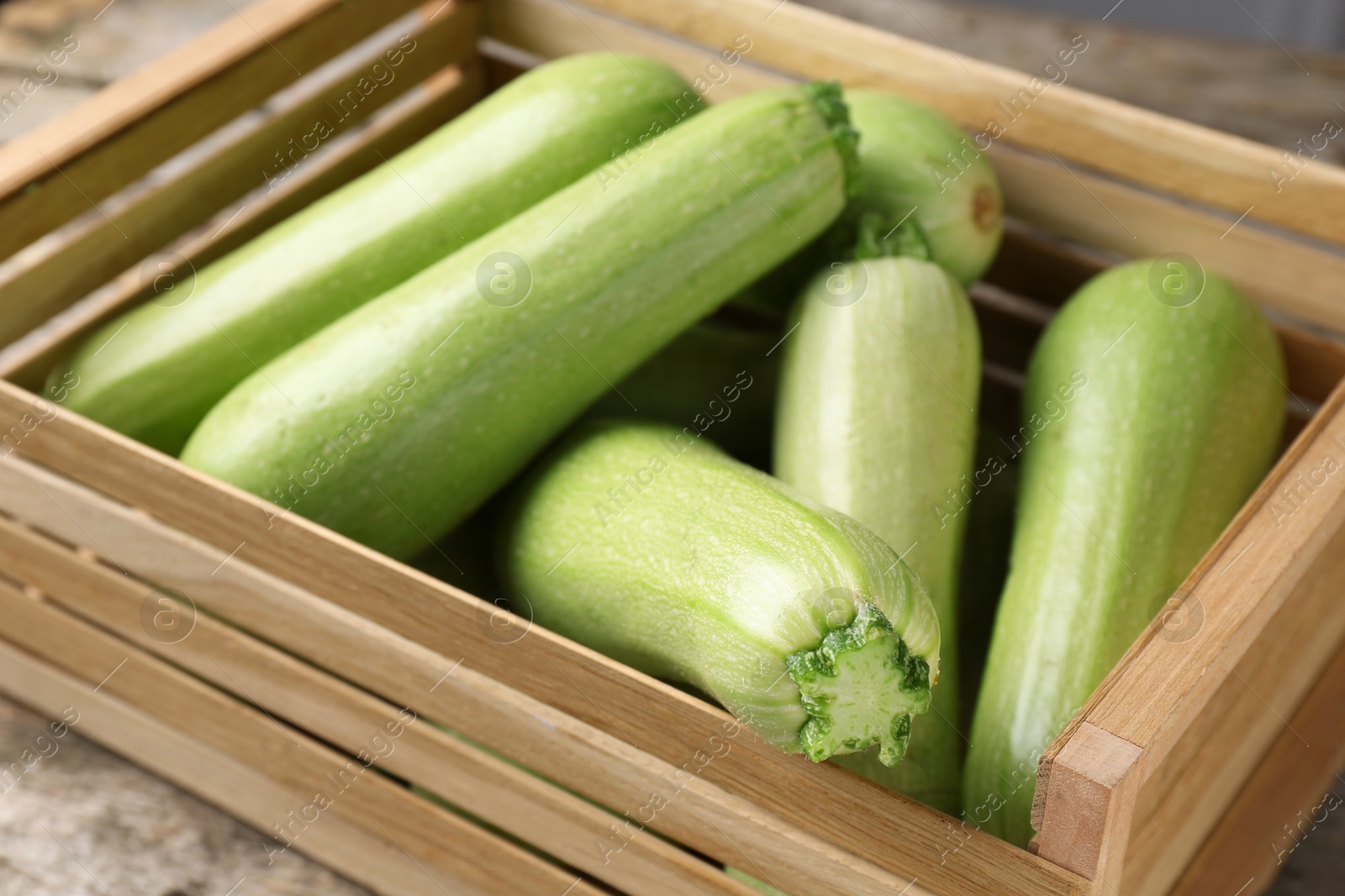 Photo of Crate with fresh zucchinis on wooden table, closeup