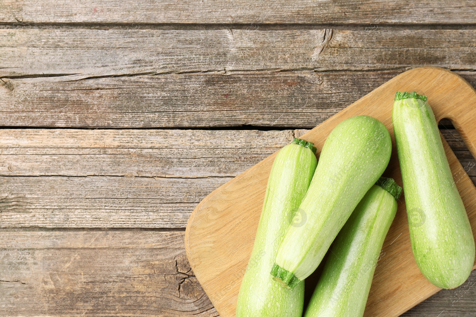 Photo of Board with fresh zucchinis on wooden table, top view. Space for text