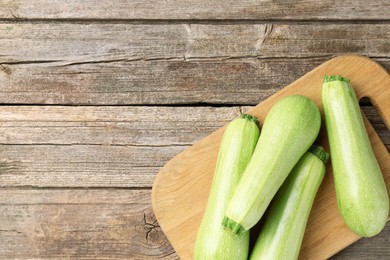 Photo of Board with fresh zucchinis on wooden table, top view. Space for text