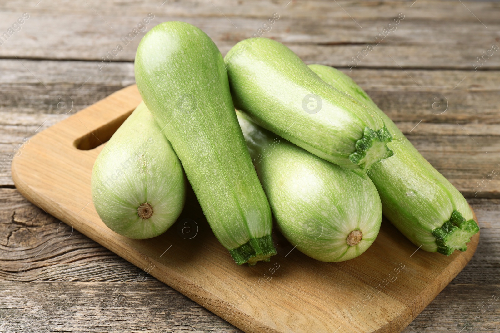 Photo of Board with fresh zucchinis on wooden table, closeup