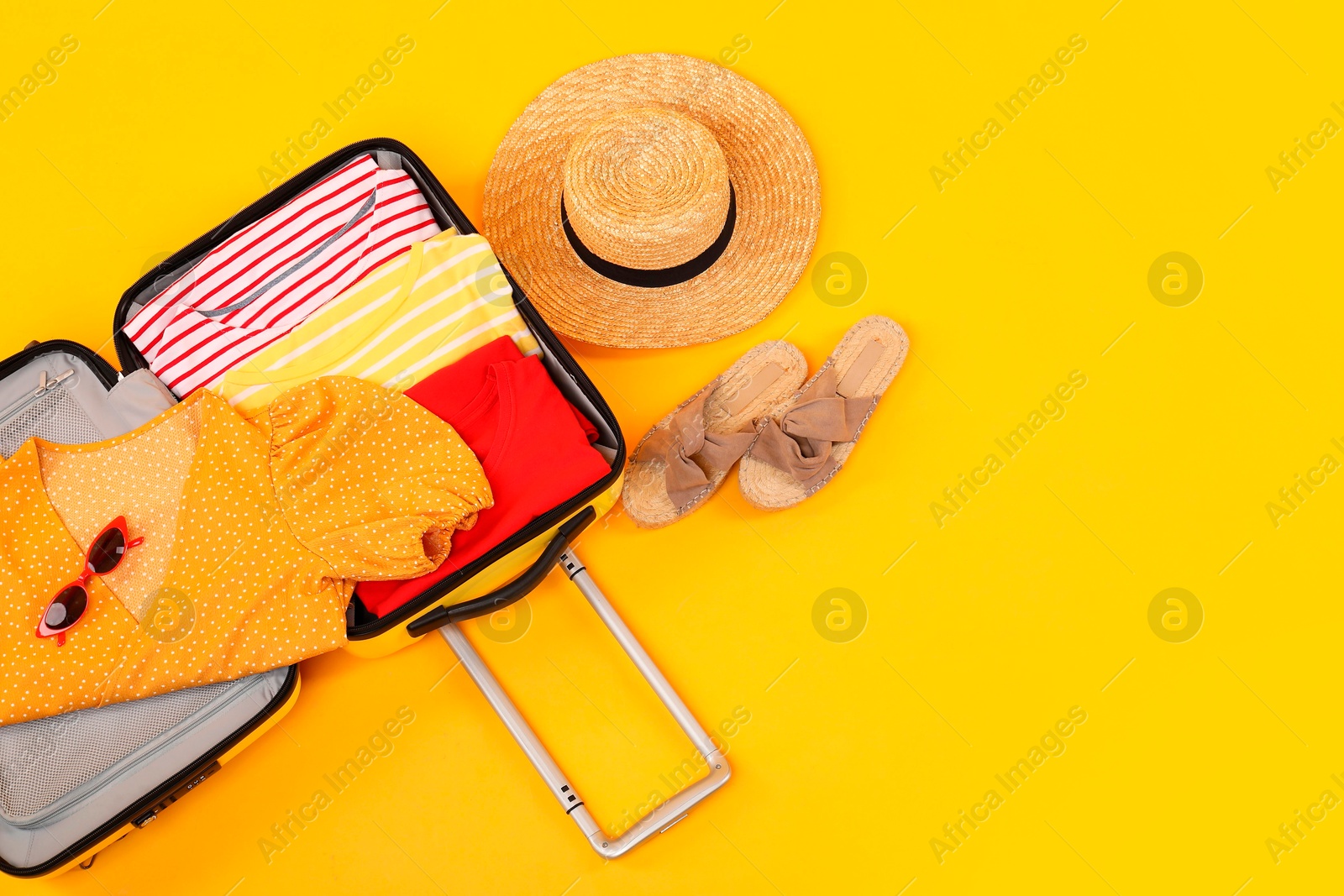 Photo of Open suitcase with clothes, wicker hat and shoes on yellow background, flat lay. Space for text