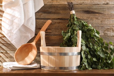 Sauna equipment. Bucket, ladle, birch whisk and towels on wooden table indoors