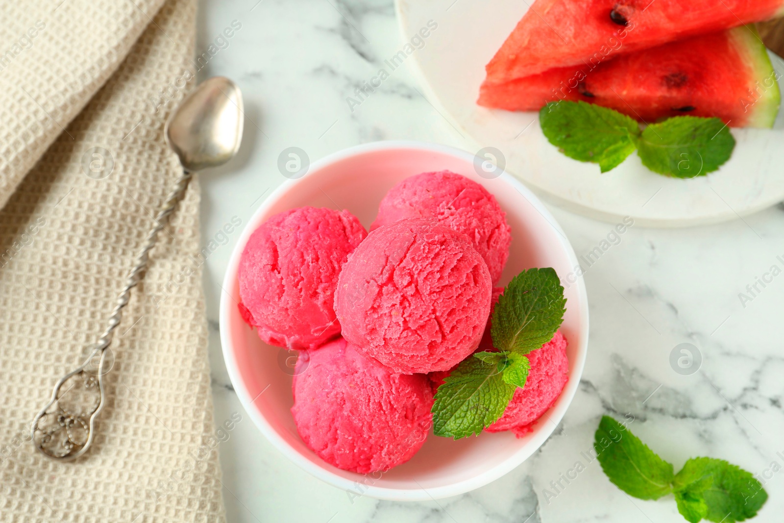 Photo of Scoops of tasty watermelon sorbet with mint in bowl and spoon on white marble table, flat lay