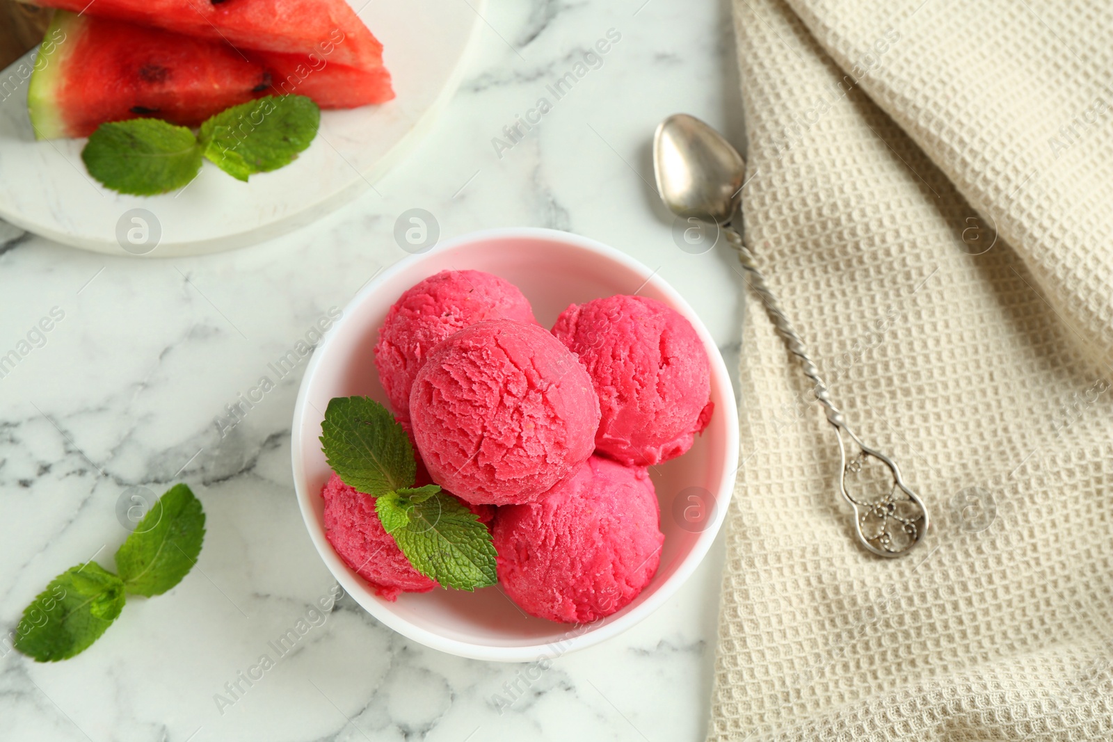 Photo of Scoops of tasty watermelon sorbet with mint in bowl and spoon on white marble table, flat lay