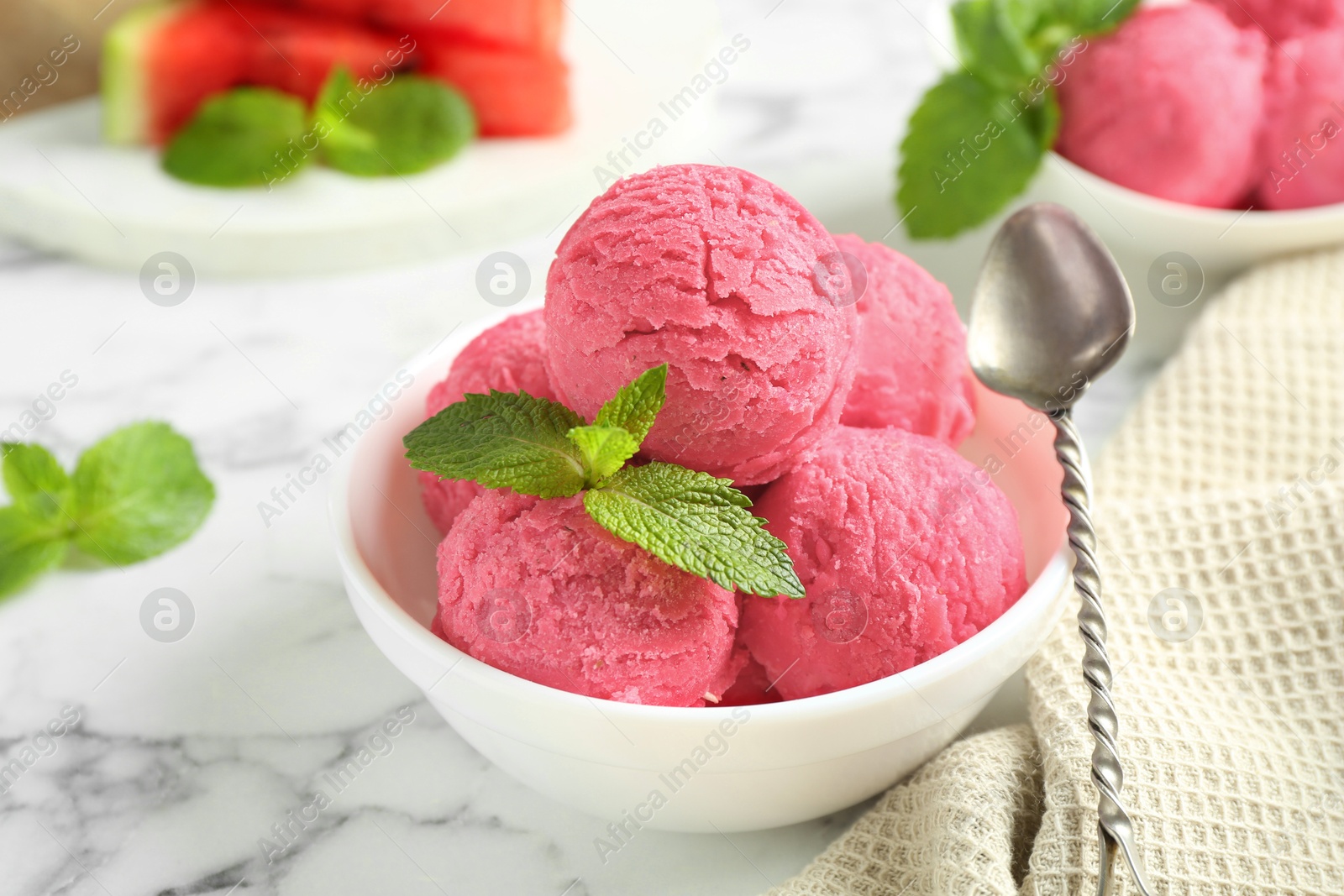 Photo of Scoops of tasty watermelon sorbet with mint in bowl and spoon on white marble table, closeup