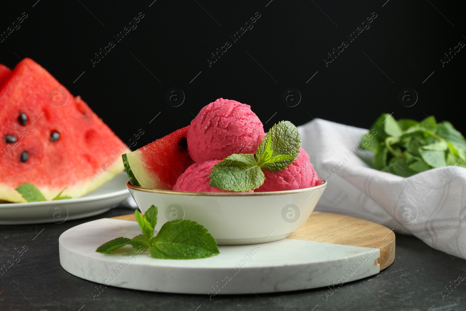 Photo of Scoops of tasty watermelon sorbet with mint and fresh fruit in bowl on grey textured table