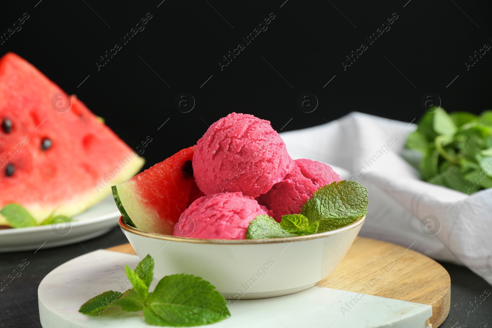 Photo of Scoops of tasty watermelon sorbet with mint and fresh fruit in bowl on grey textured table, closeup