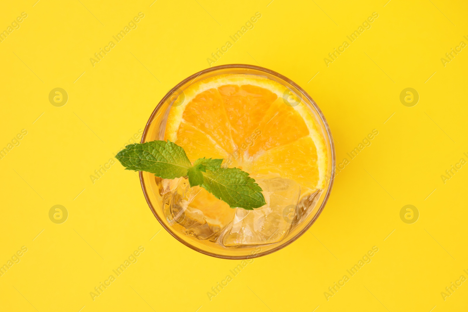 Photo of Refreshing water with orange and mint in glass on yellow background, top view