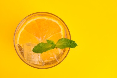 Refreshing water with orange and mint in glass on yellow background, top view. Space for text