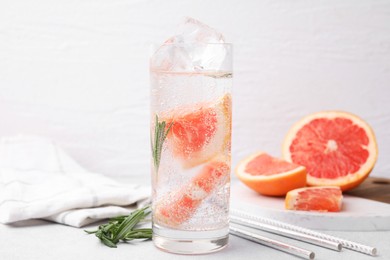 Photo of Refreshing water with grapefruit and rosemary in glass on light table