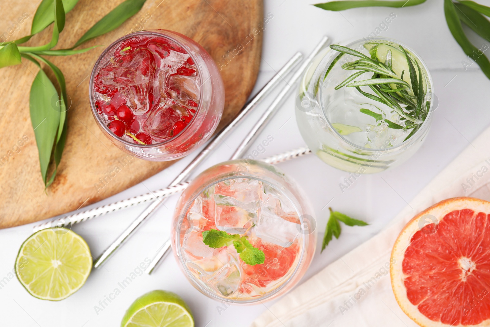 Photo of Different refreshing drinks in glasses on white tiled table, flat lay