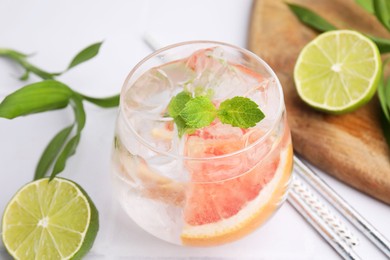 Photo of Refreshing water with grapefruit and mint in glass on white table, closeup