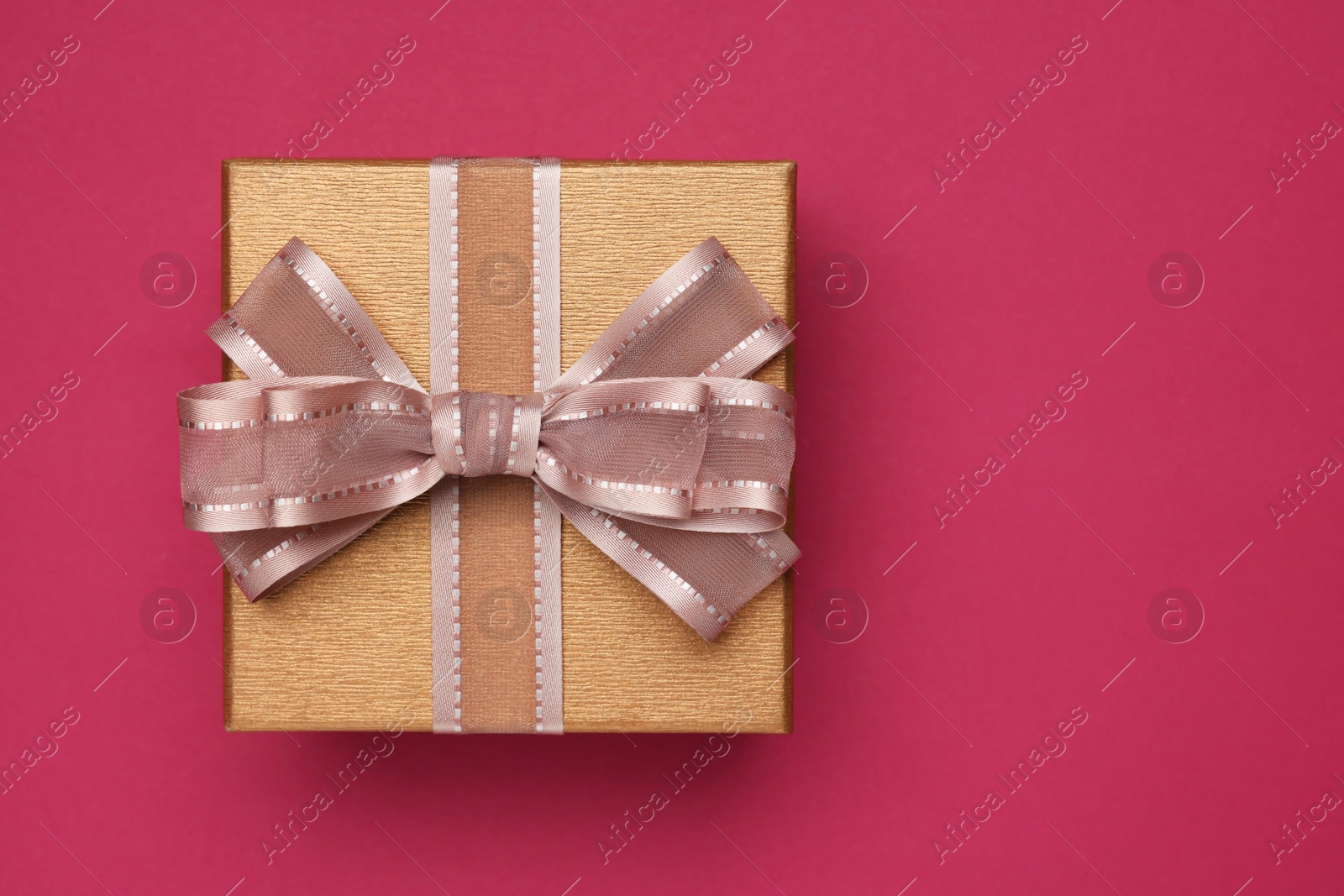 Photo of Gift box with bow on burgundy background, top view. Space for text