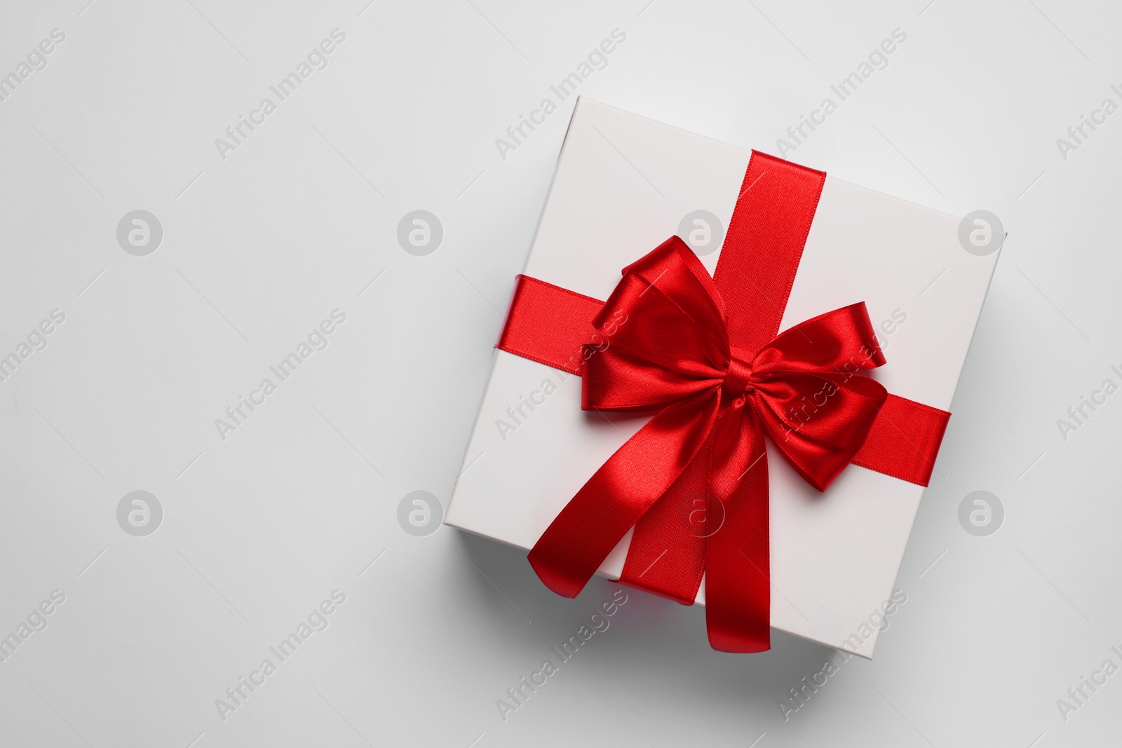 Photo of Gift box with red bow on light grey background, top view. Space for text