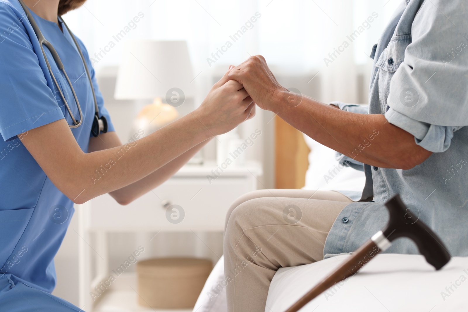 Photo of Young healthcare worker supporting senior patient indoors, closeup