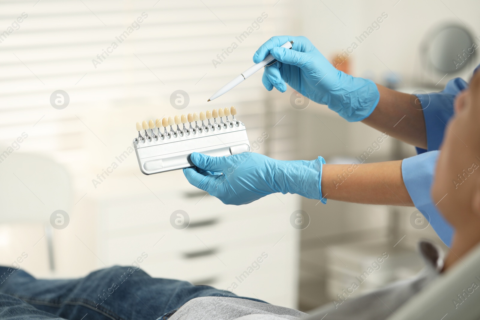 Photo of Doctor and patient choosing shade on teeth color palette in clinic, closeup. Dental veneers