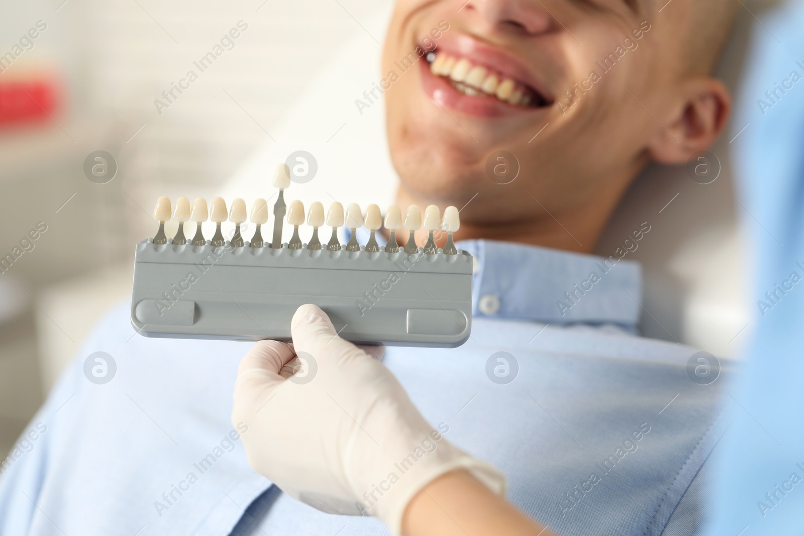 Photo of Doctor checking young man's teeth color in clinic, closeup. Dental veneers