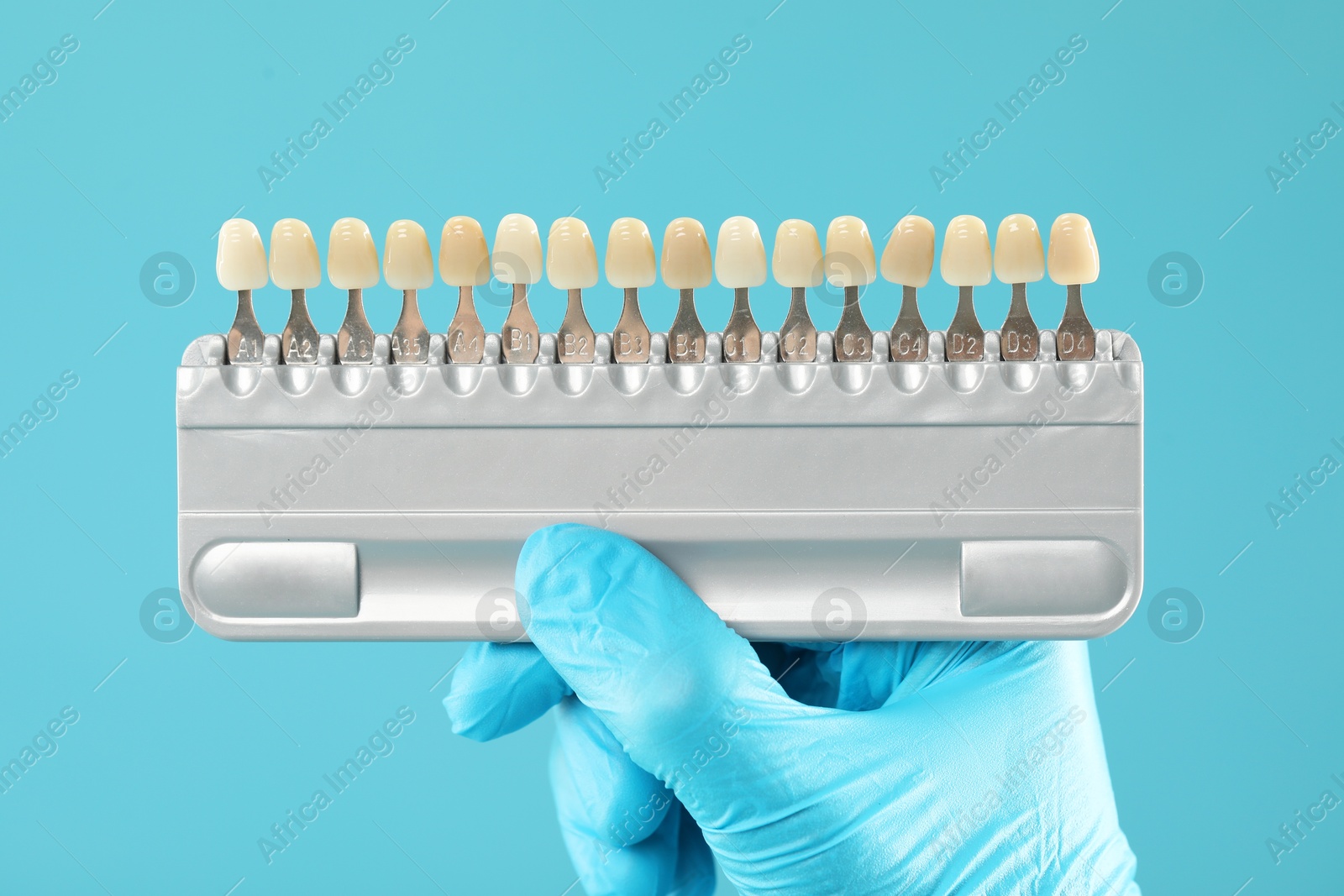 Photo of Doctor with teeth color chart on light blue background, closeup. Dental veneers