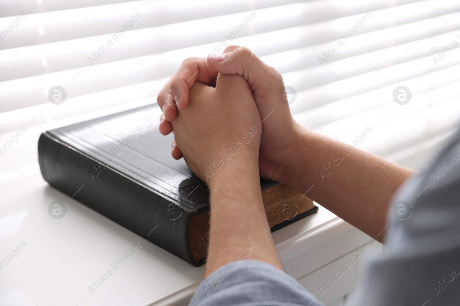 Photo of Man with Bible praying at white table, closeup