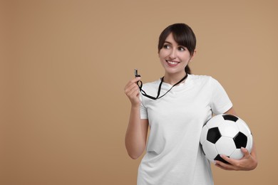 Photo of Happy woman with whistle and soccer ball on beige background, space for text