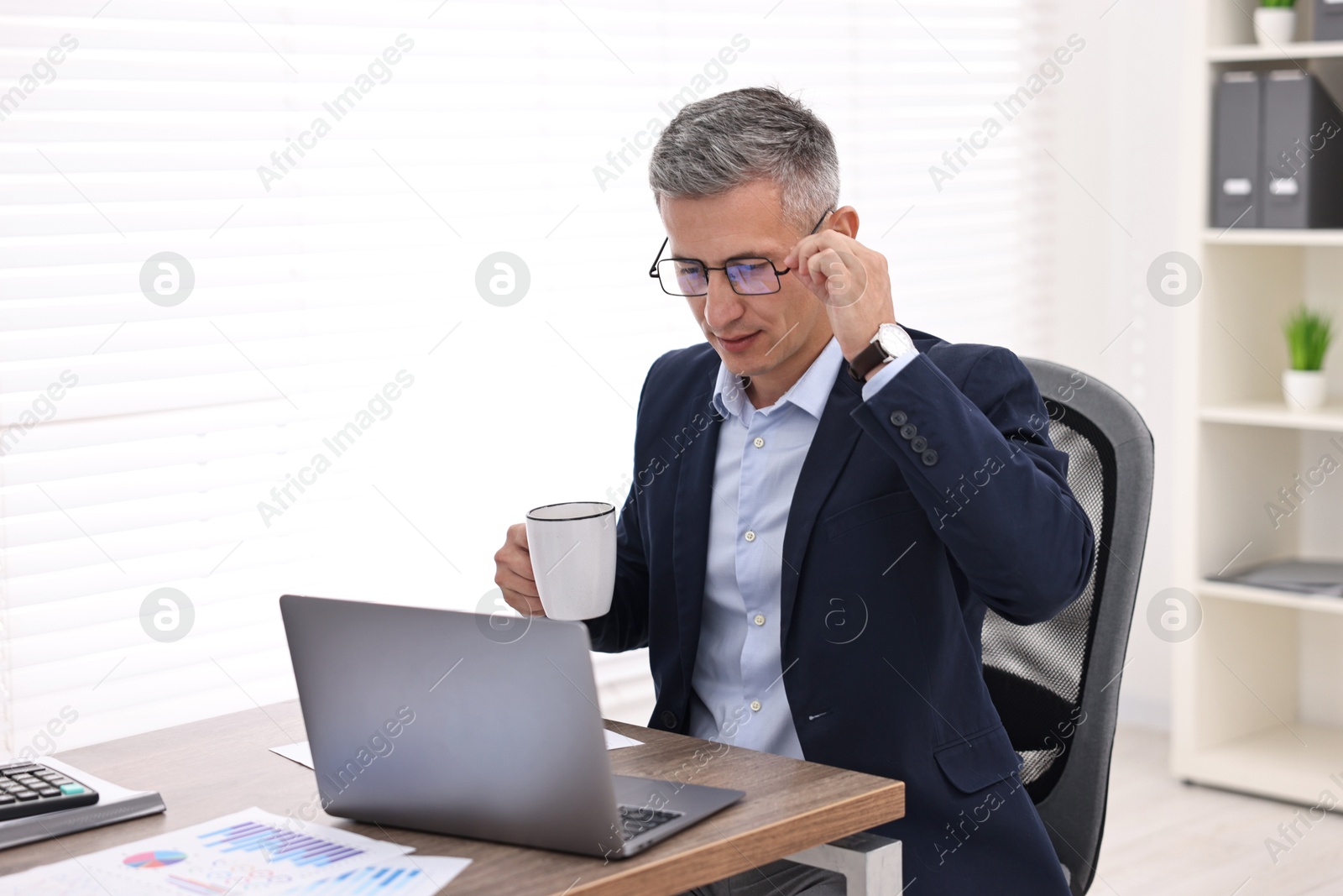 Photo of Banker with cup and laptop at wooden table in office