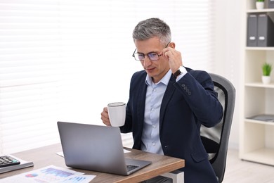 Photo of Banker with cup and laptop at wooden table in office