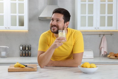 Happy man holding glass of water with lemon in kitchen