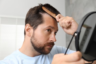 Photo of Man brushing his hair near mirror indoors. Alopecia problem